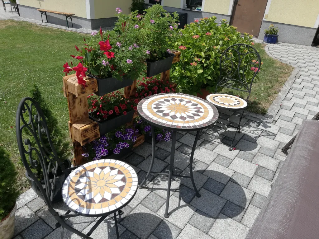 Sitzplatz mit Mosaiktischen und Blumen vor dem Haus