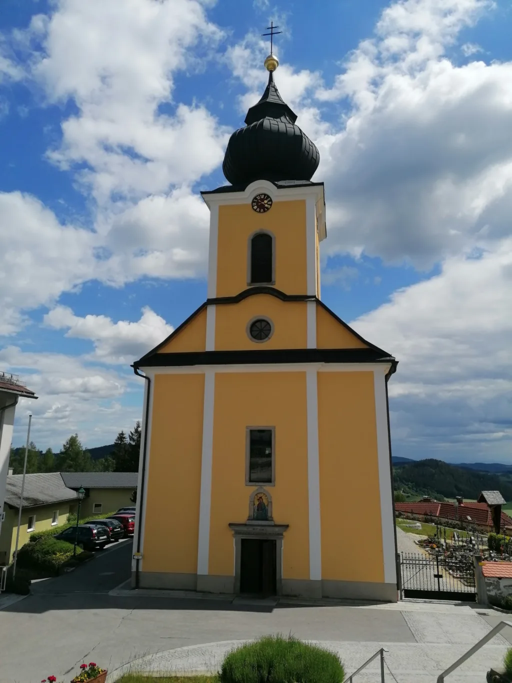 Gelbe Pfarrkirche mit Zwiebelturm unter blauem Himmel