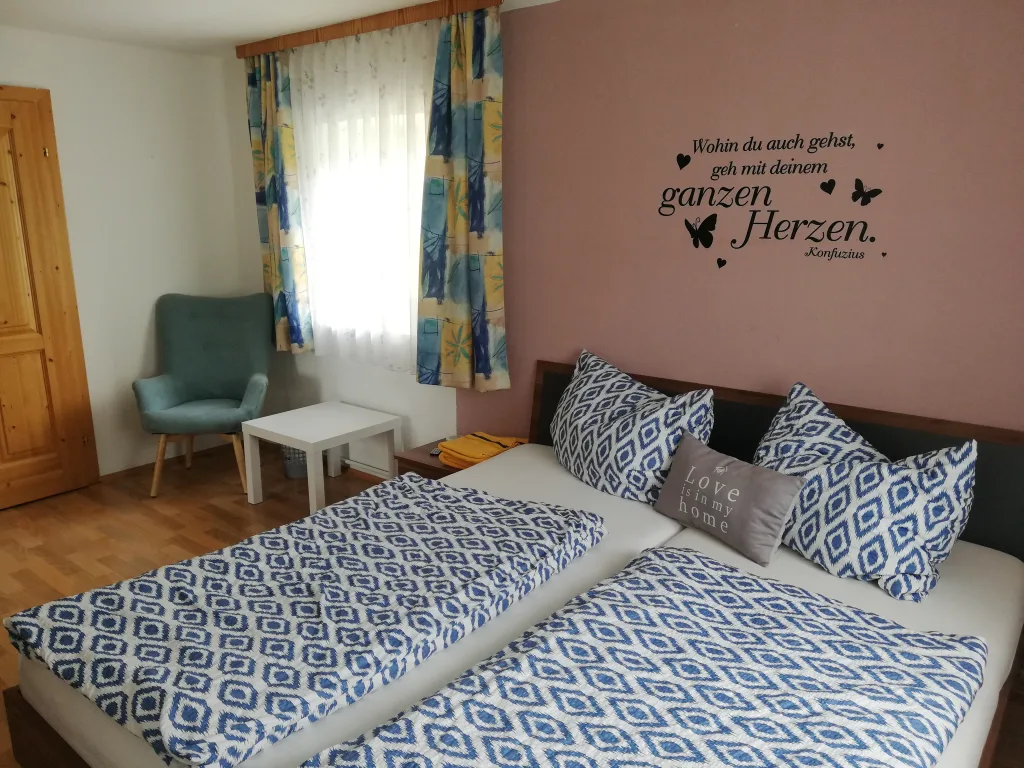 Doppelzimmer mit Doppelbett, blau gemusterter Bettwäsche und Lesesessel am Fenster